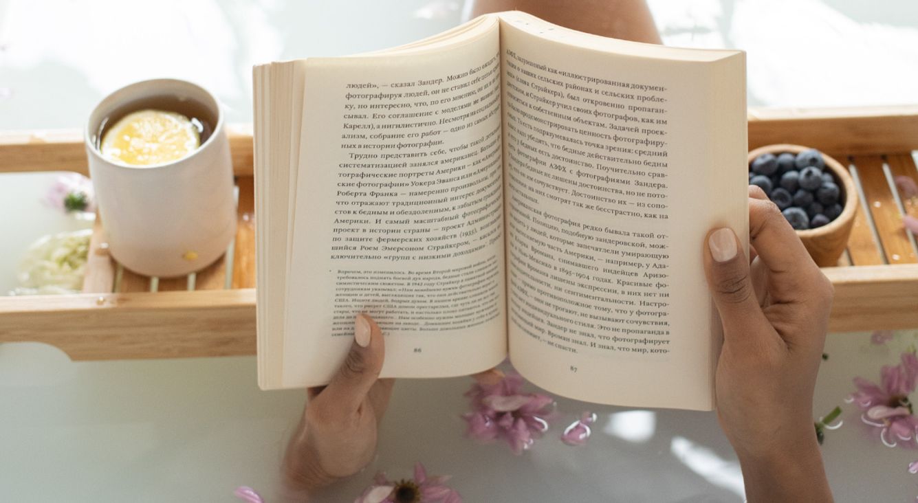 Person hält Buch in Badewanne neben Teetasse