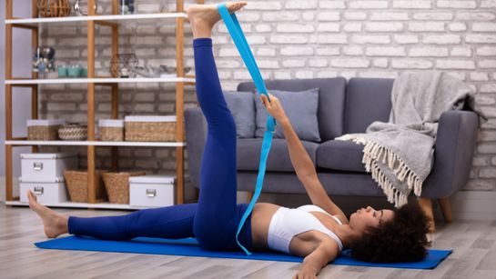 Person bei Übung mit Yoga-Gurt mit gestrecktem Bein - Foto: canva.com