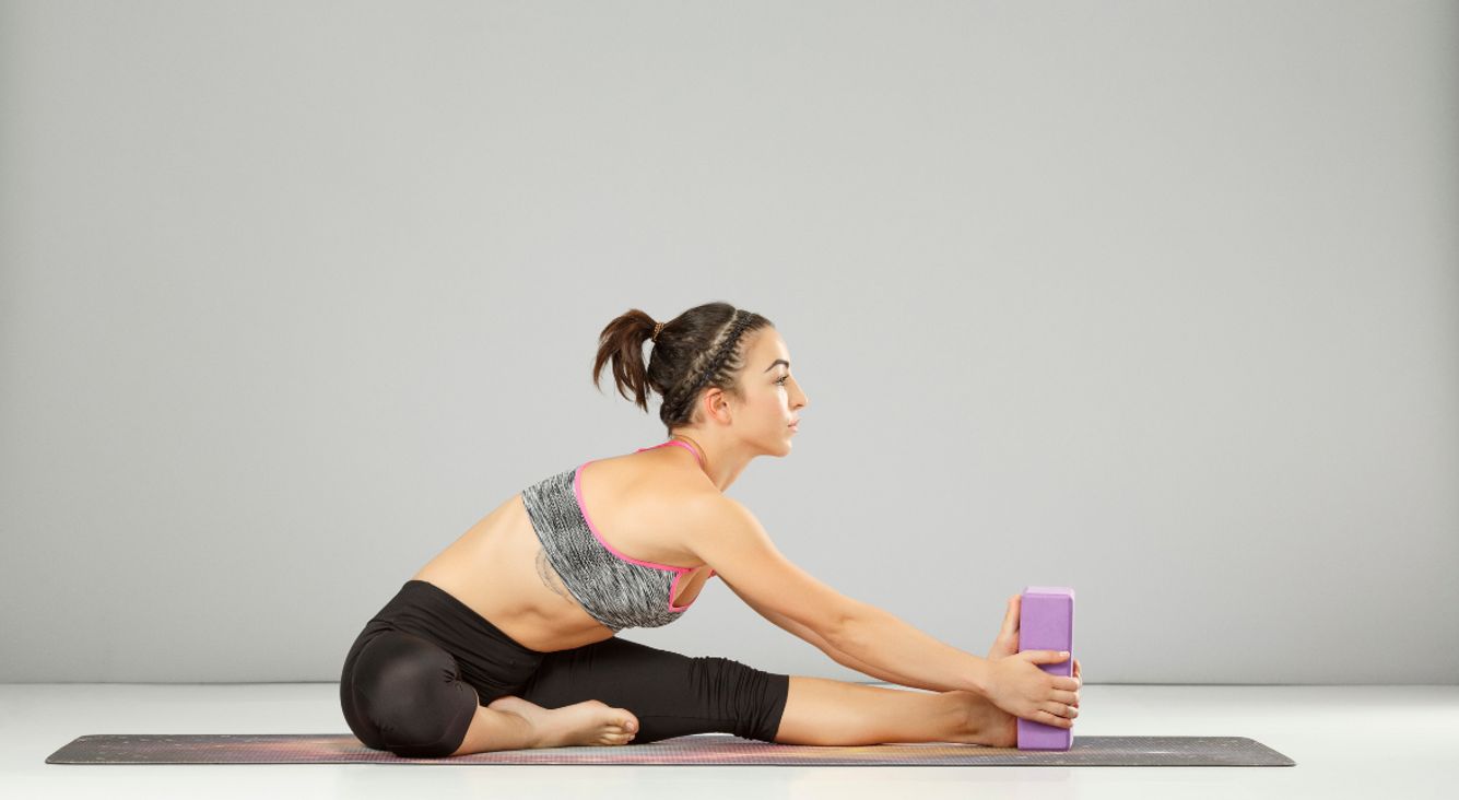 Person bei sitzender Vorbeuge mit Yoga-Block