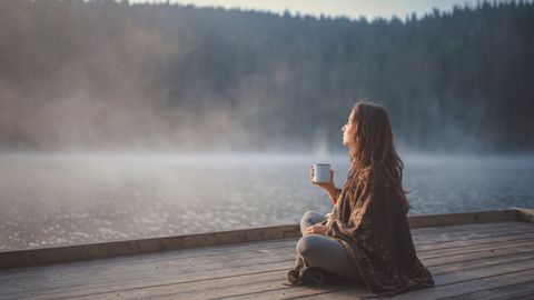 Frau sitzt auf Steg mit Tasse - Foto: canva.com