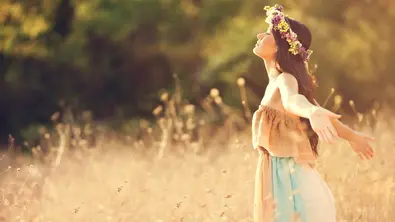 Person mit Blumenkranz in Feld - Foto: canva.com