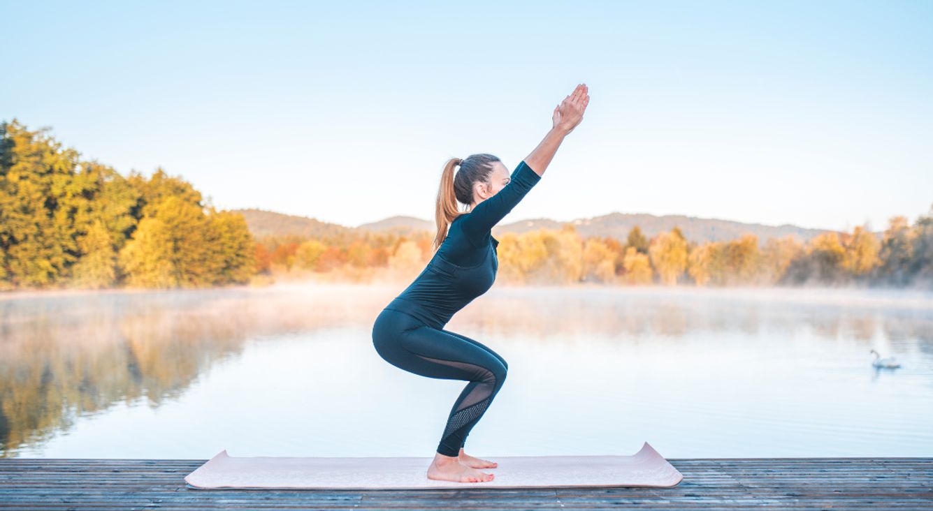 Frau in Stuhlpose auf Yogamatte vor See