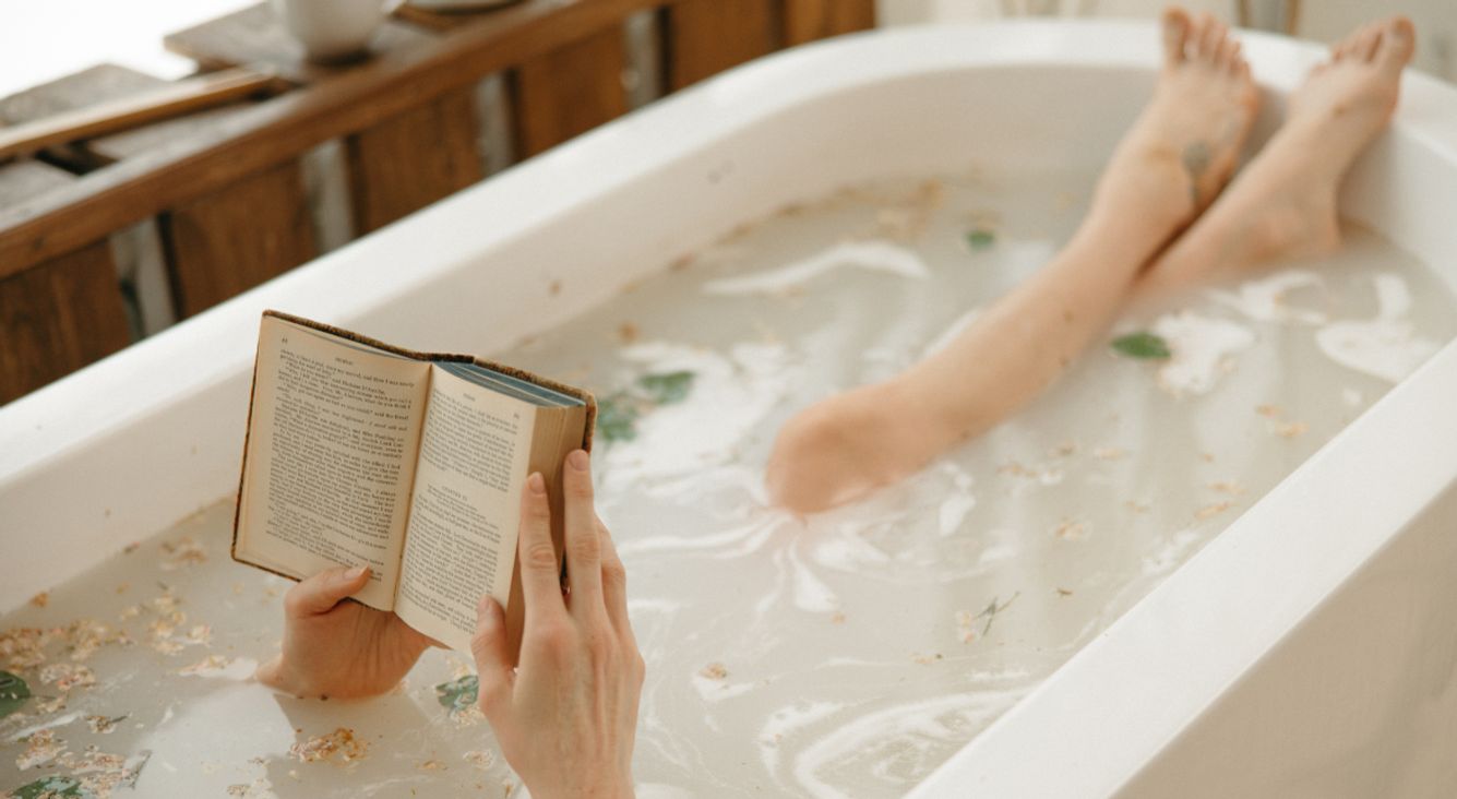 Person in Badewanne mit Buch und Badezusätzen
