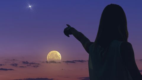 Eine Frau steht vor dem Vollmond und streckt den Arm in Richtung des Mondes aus. - Foto: canva.com