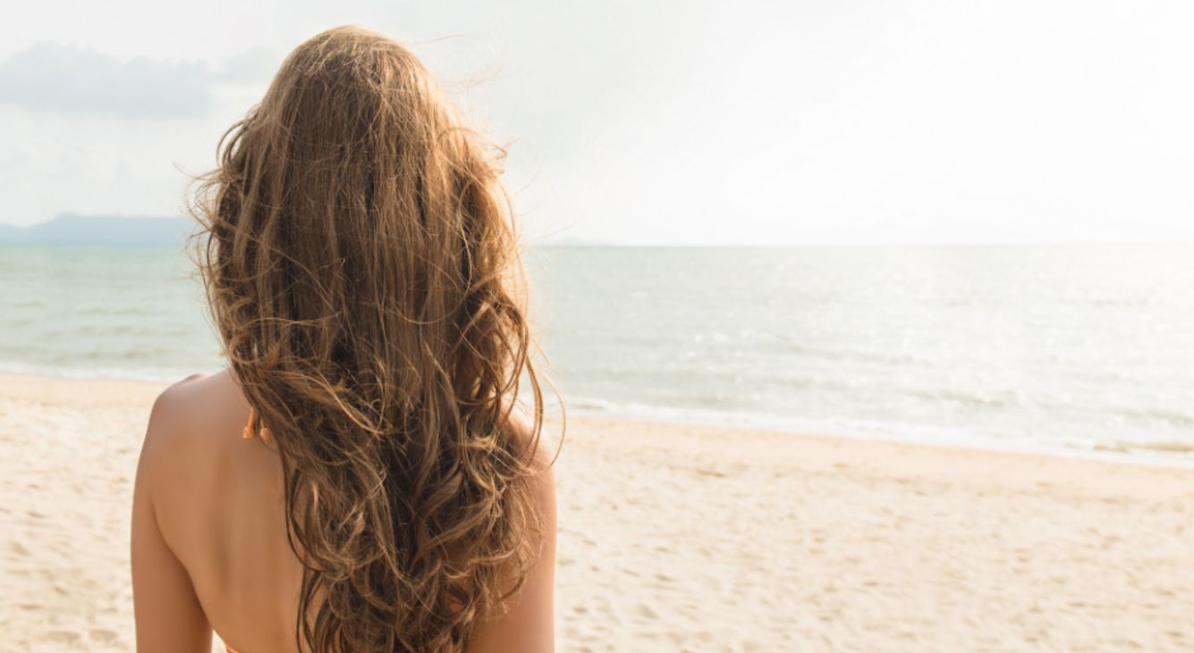 Frau am Strand guckt zum Meer