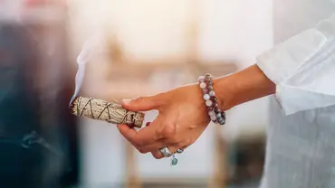 weibliche Hand mit Armbändern und einem Räucherbündel weißer Salbei - Foto: canva.com weibliche Hand mit Armbändern und einem Räucherbündel weißer Salbei - Foto: canva.com