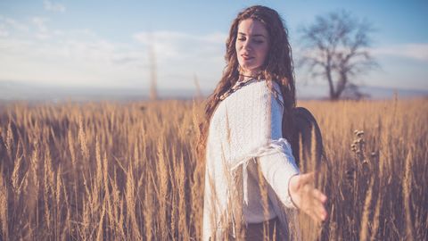 Frau steht mit geöffneten Armen im Kornfeld - Foto: canva.com