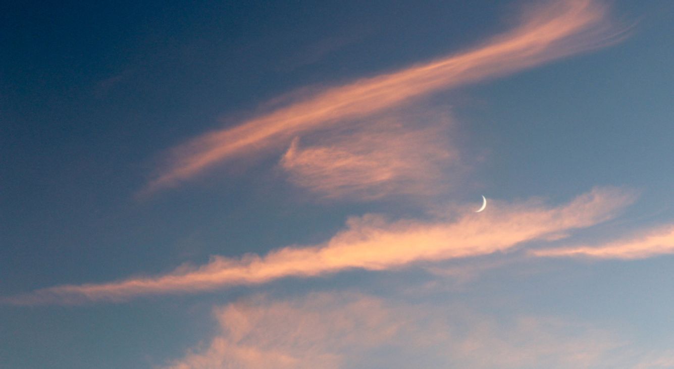 Neumond am blauen Himmel mit rosa Wolken