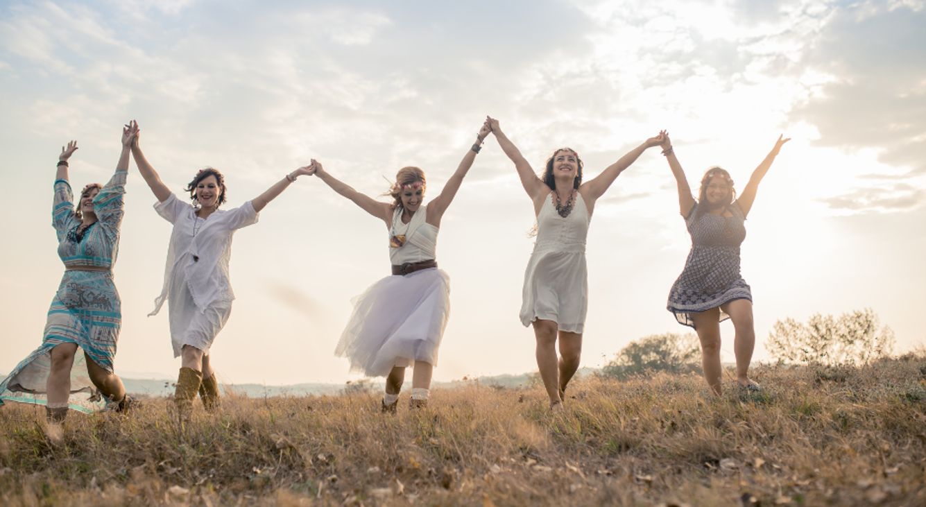 Fünf Frauen halten sich an den Händen und laufen über eine Wiese