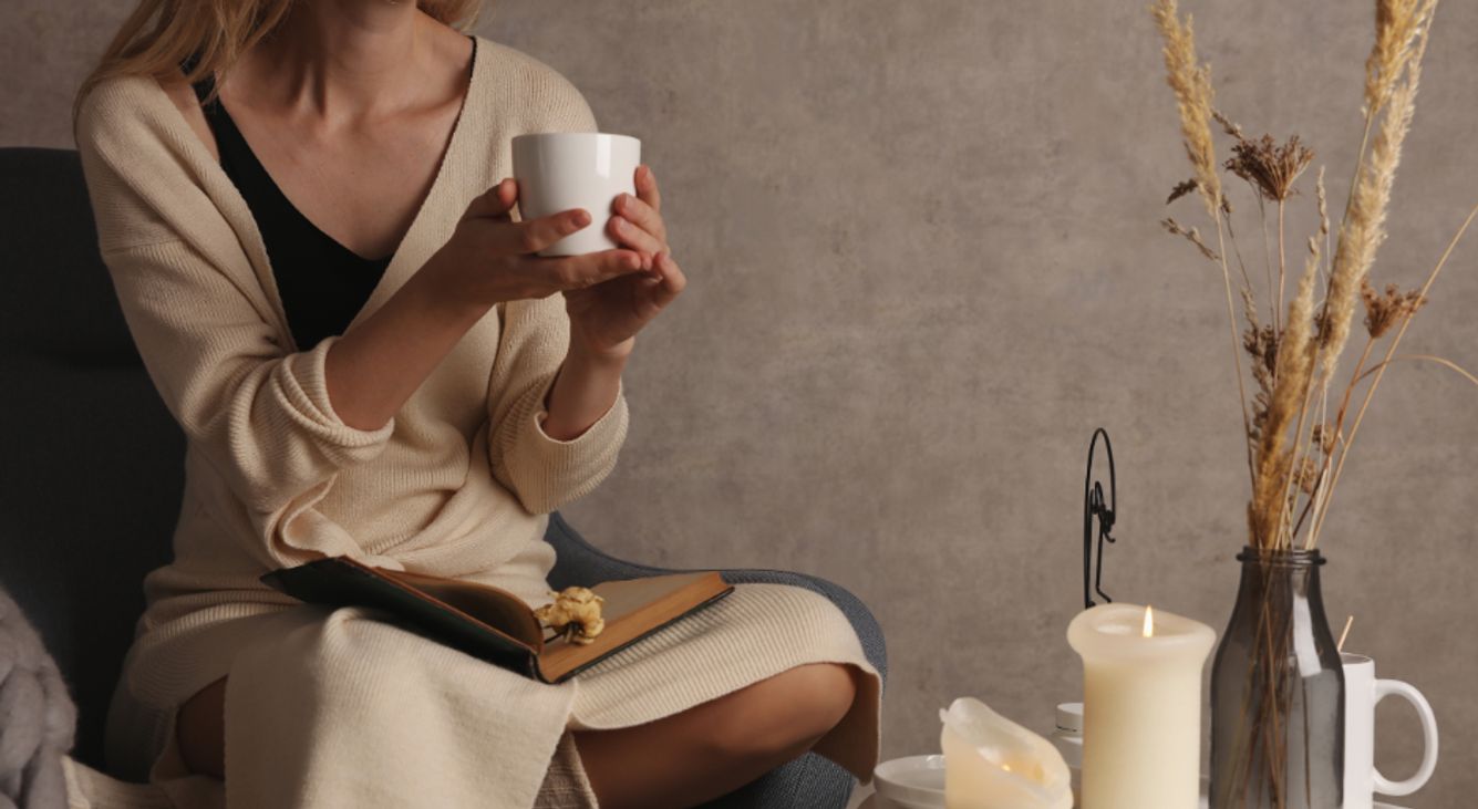 Frau mit Teetasse in der Hand vor gemütlichem Setting mit Kerze