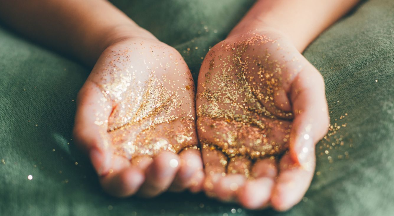 Offene Hände auf grün mit Goldstaub darin