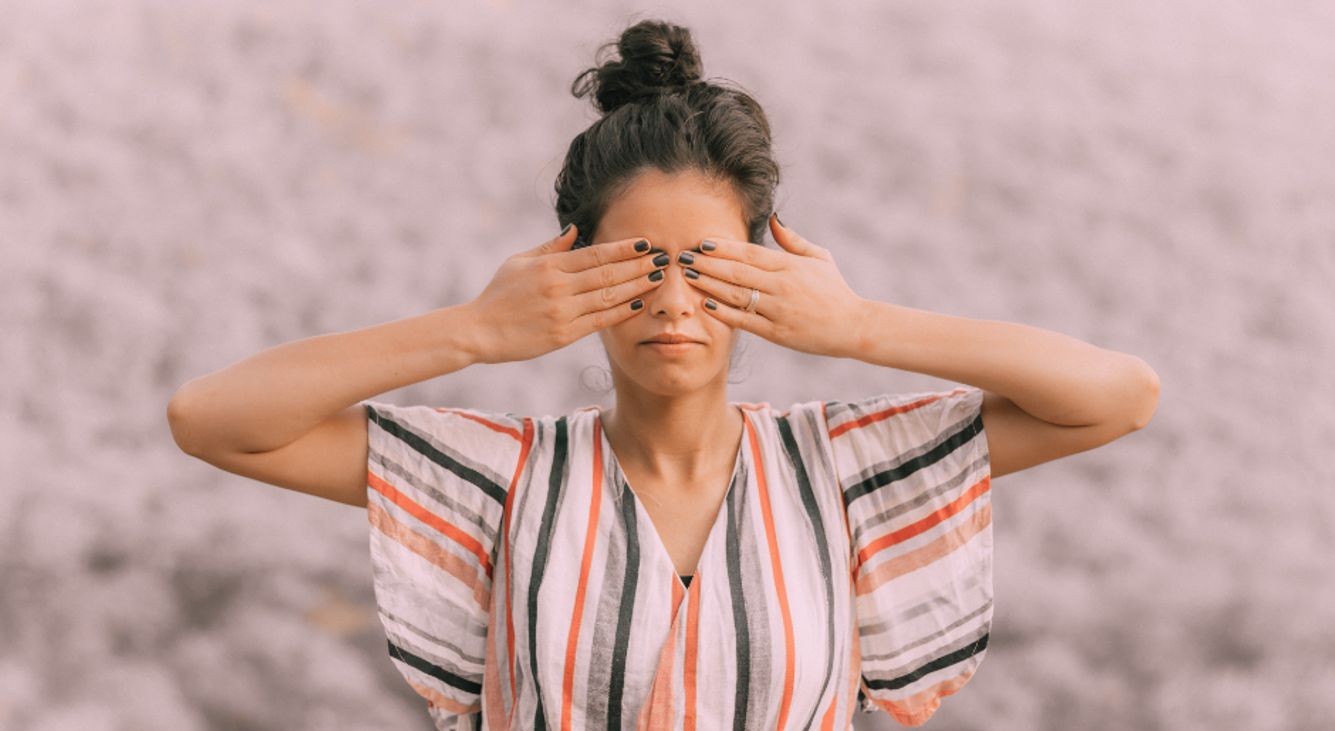 Frau in der Natur hält sich die Finger über die Augen