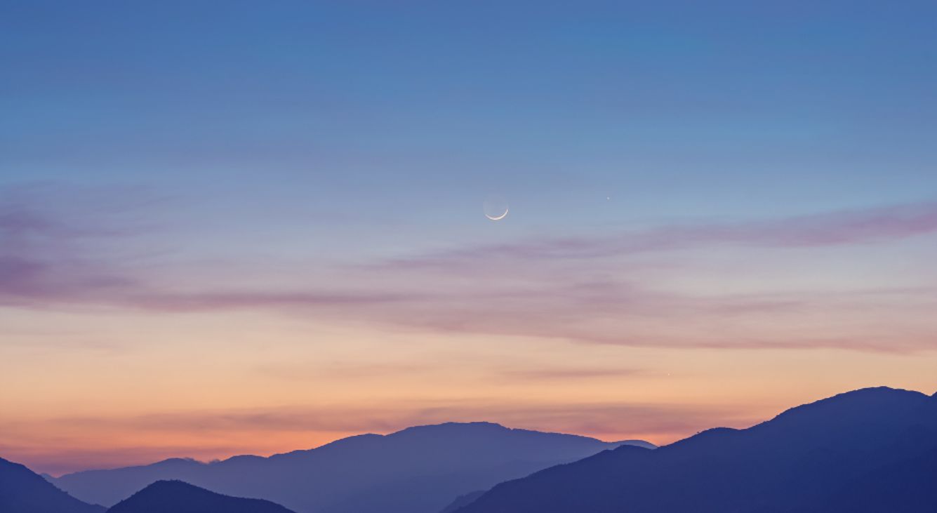 Neumond am Himmel über Bergen