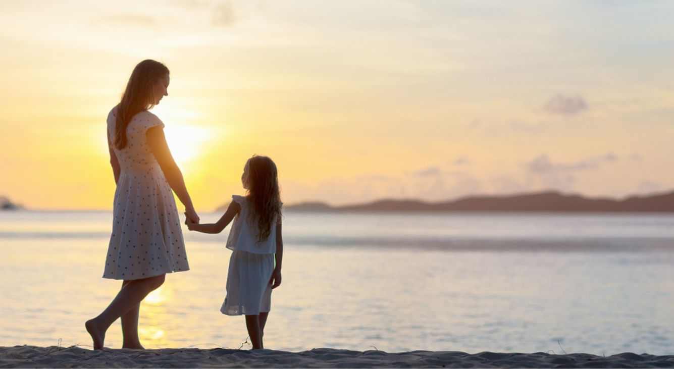 Eine Mutter läuft mir ihrer Tochter am Strand, während im Hintergrund die Sonne untergeht.