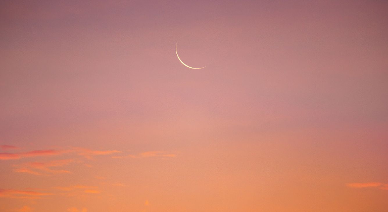 Ein Neumond am rosa erleuchteten Himmel