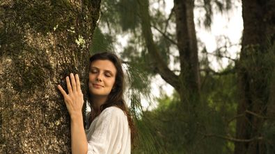 Frau lehnt mit geschlossenen Augen am Baum - Foto: canva.com