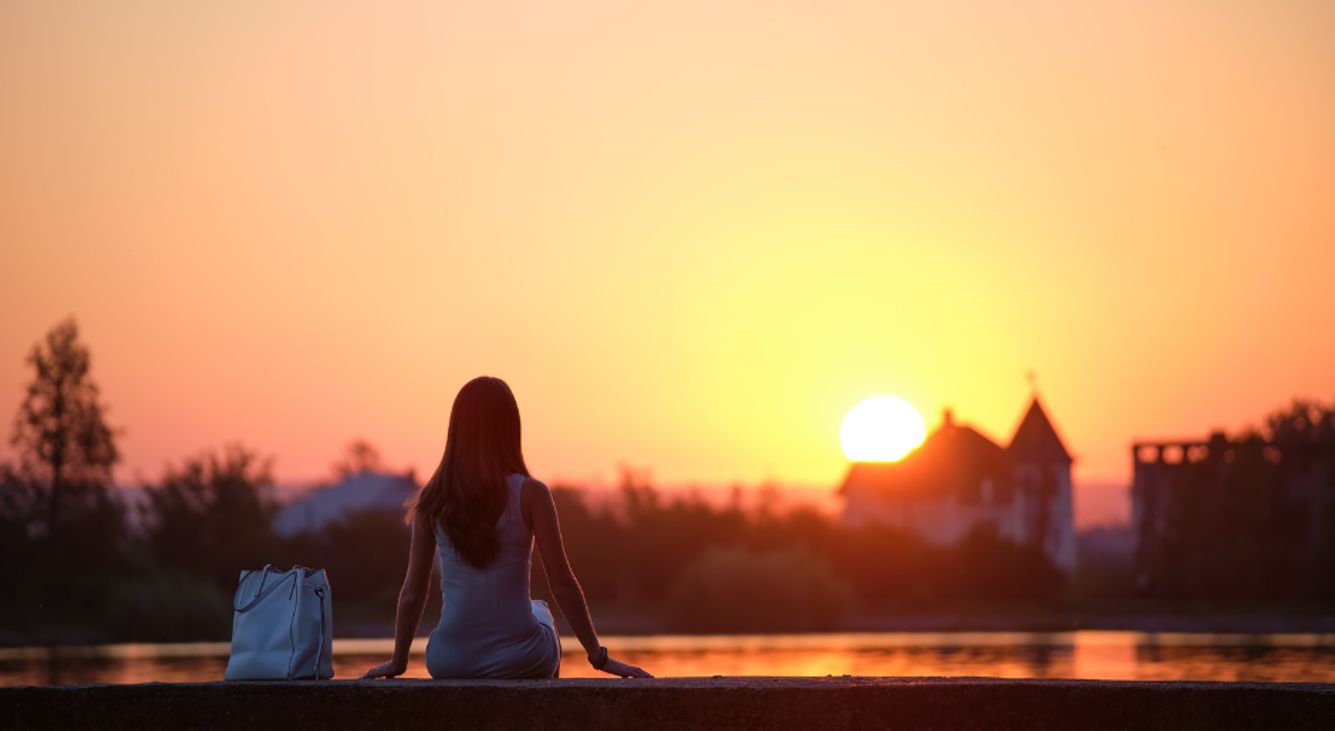 Einsame Frau sitzt an einem See und schaut den Sonnenuntergang