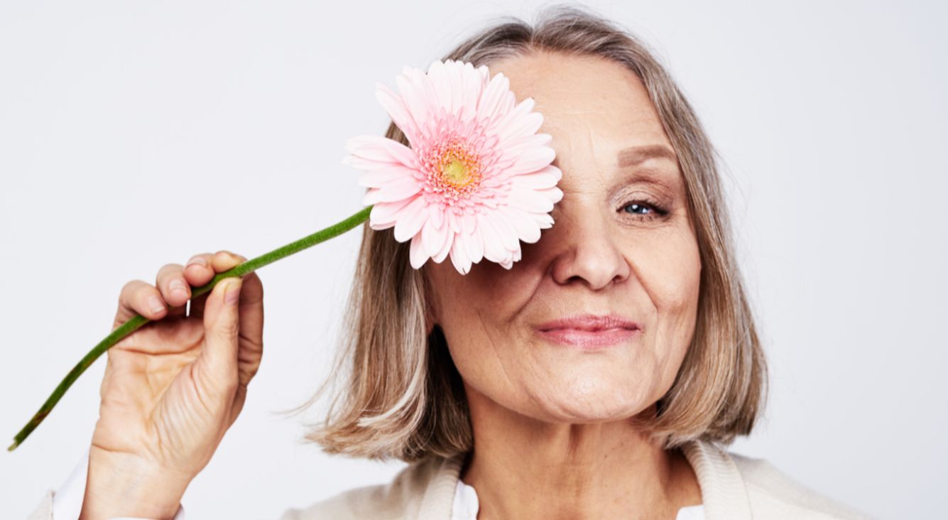 Ältere Frau hält Blume vor Auge
