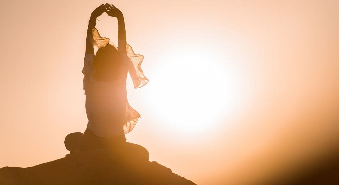 Frau meditiert beim Sonnenuntergang auf einem Stein