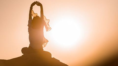 Frau meditiert beim Sonnenuntergang auf einem Stein - Foto: Getty Images  / pepmiba
