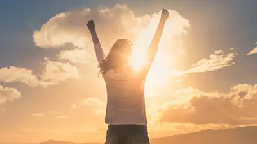 Frau streckt Arme in die Luft vor Sonne und Himmel - Foto: Canva.com