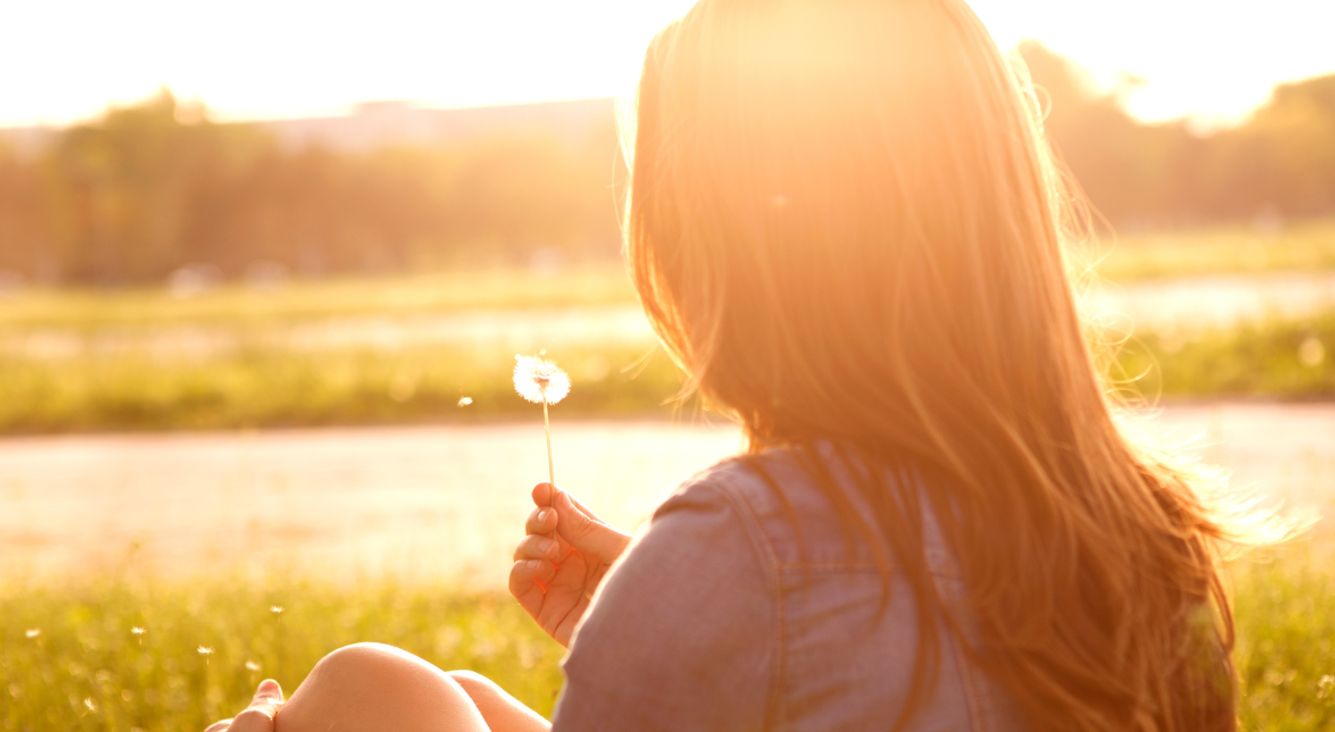 Frau sitzt in Wiese mit Pusteblume