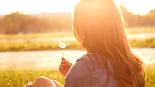 Frau sitzt in Wiese mit Pusteblume - Foto: canva.com