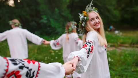 Frauen mit Blumenkränzen tanzen im Kreis - Foto: Canva.com