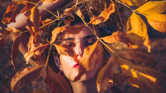 Frau hält Ast mit Herbstblättern vor Gesicht - Foto: canva.com