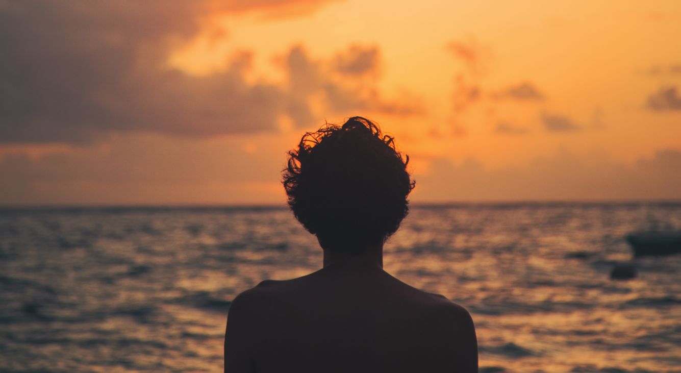 Person steht am Meer und blickt auf einen Sonnenuntergang.