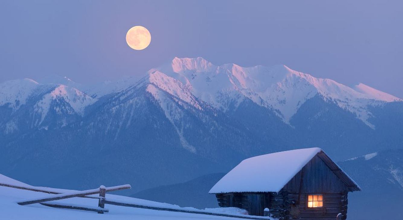 Vollmond in den Bergen bei Schnee und mit Holzhütte