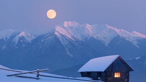 Vollmond in den Bergen bei Schnee und mit Holzhütte - Foto: canva.com