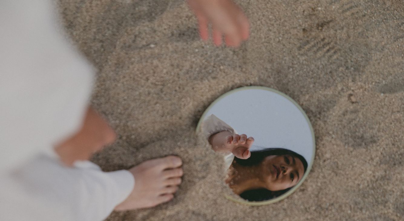 Frau sieht in Spiegel im Sand
