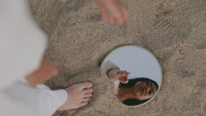Frau sieht in Spiegel im Sand - Foto: Canva.com