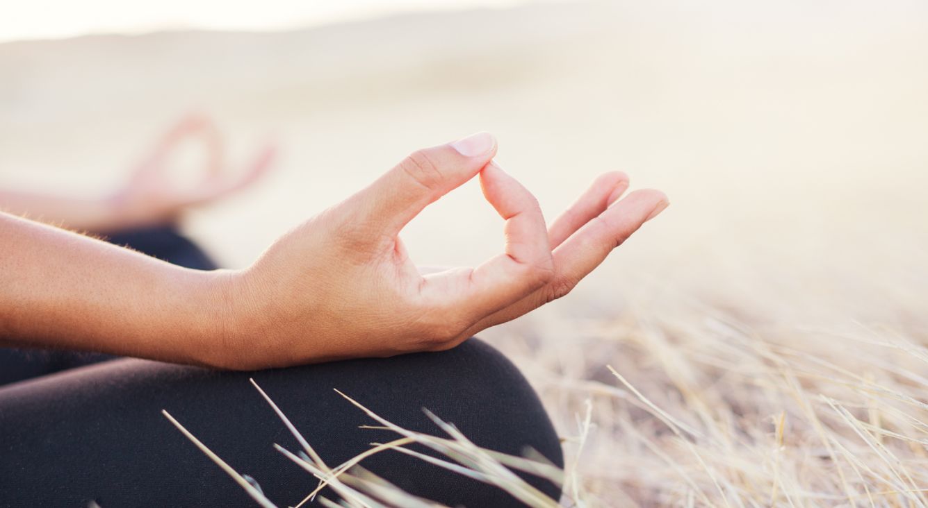 Spirituelle Selbstfürsorge: So schenkest du deinem höheren Selbst mehr Aufmerksamkeit Person beim Meditieren in Feld