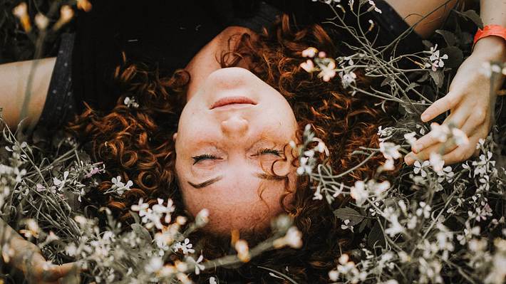 Frau liegt auf einer Blumenwiese  - Foto: Rodolfo Sanches Carvalho / Unsplash 