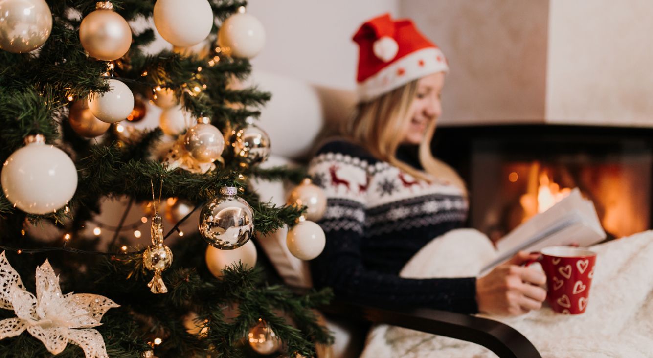 Person sitzt neben Weihnachtsbaum und liest