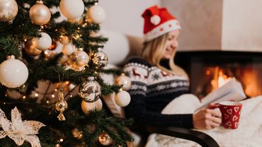 Person sitzt neben Weihnachtsbaum und liest - Foto: Canva.com