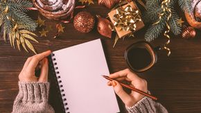 Person schreibt auf Block neben Weihnachtsdeko - Foto: Canva.com