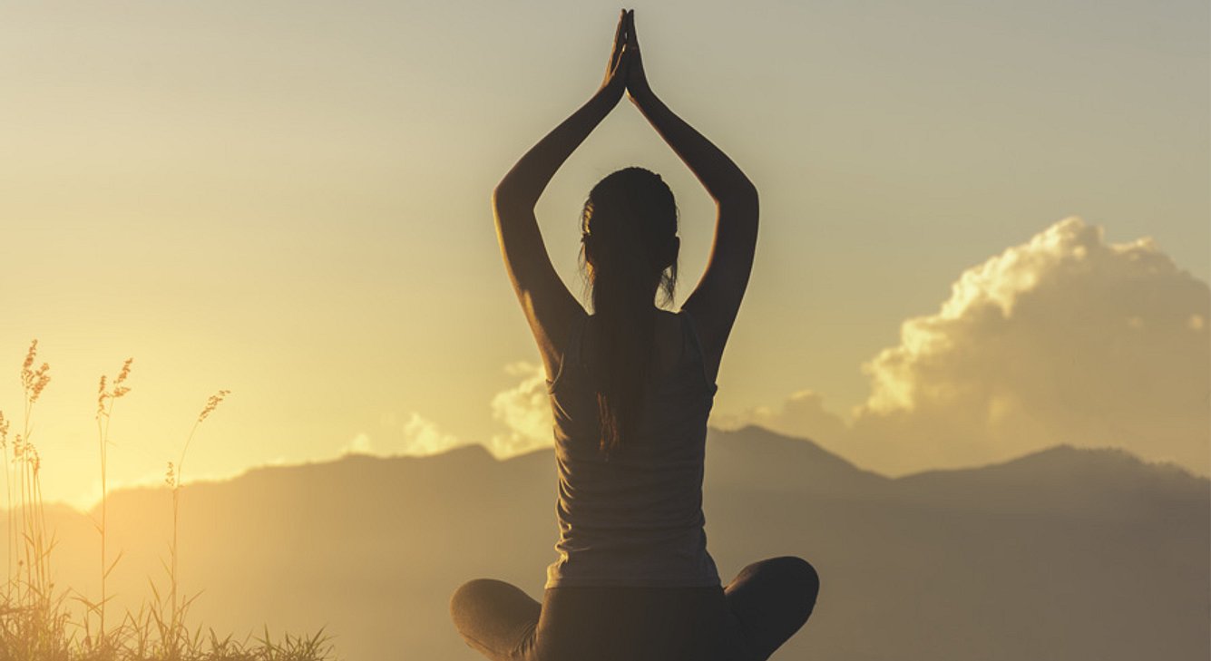 Frau in Yoga-Pose auf einer Wiese bei Sonnenaufgang