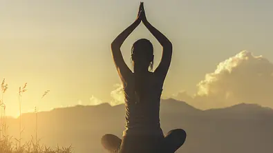 Frau in Yoga-Pose auf einer Wiese bei Sonnenaufgang