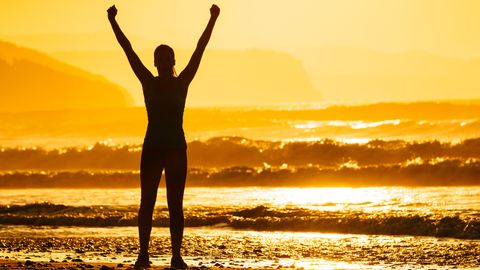 Person steht an Strand und streckt Arme in die Luft - Foto: Canva.com